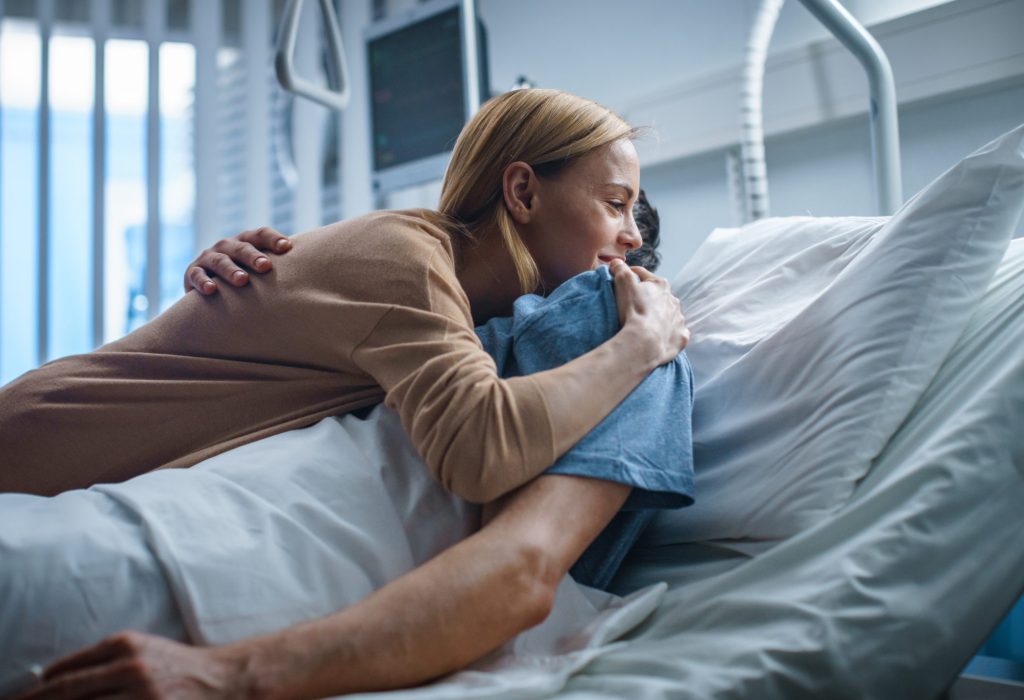 In the Hospital, Happy Wife Visits Her Recovering Husband who is Lying on the Bed. They Lovingly Embrace and Smile.